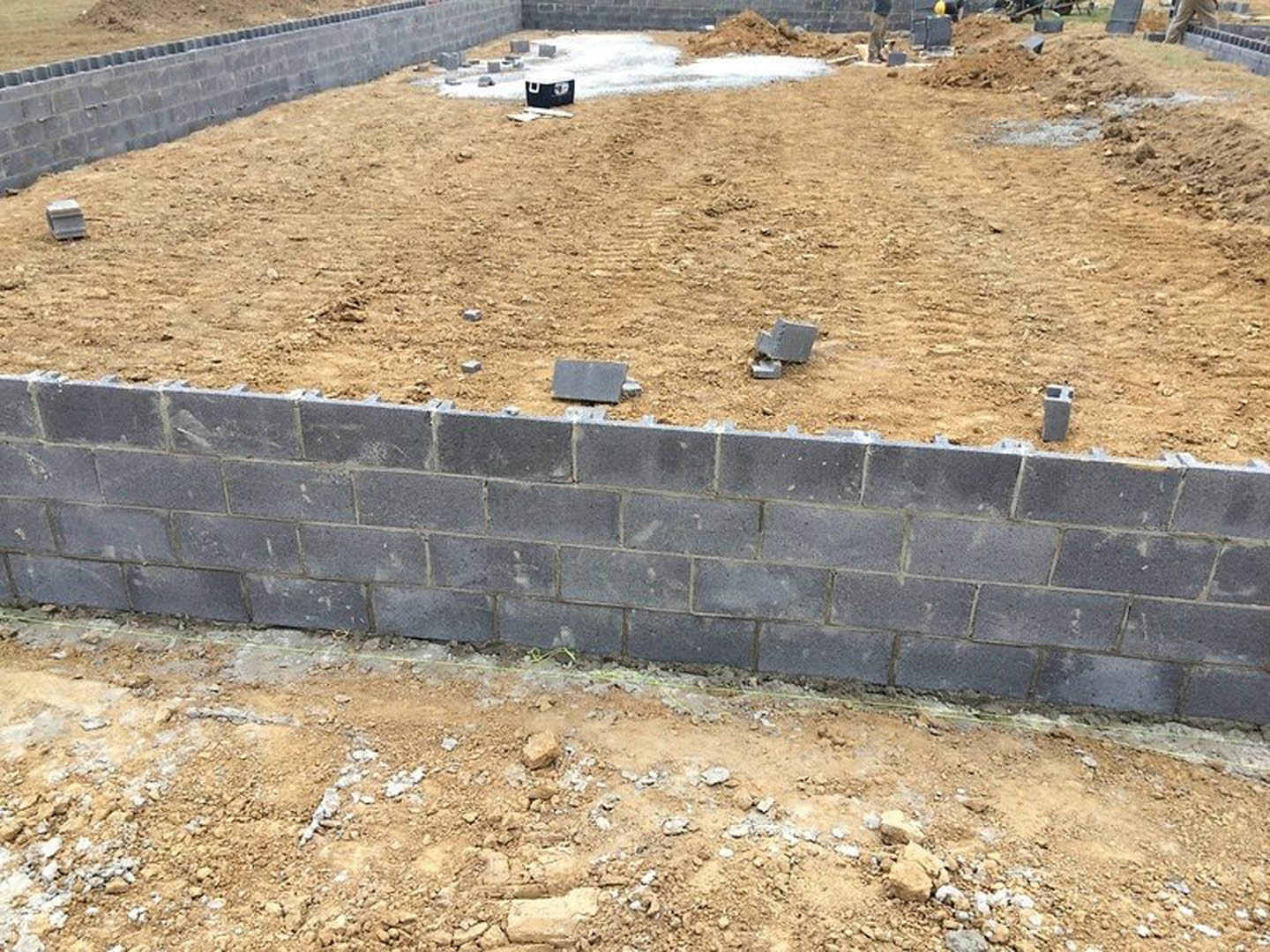 Grey brick wall partially built on a dirt construction site, surrounded by rocks, soil, and scattered building materials.