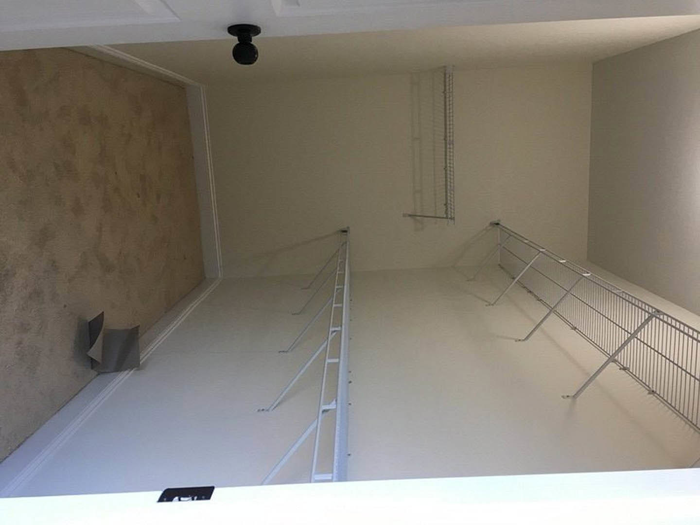 White plaster walls and ceiling, light wood flooring, white metal ladder-style railing, metal shelving rack against wall