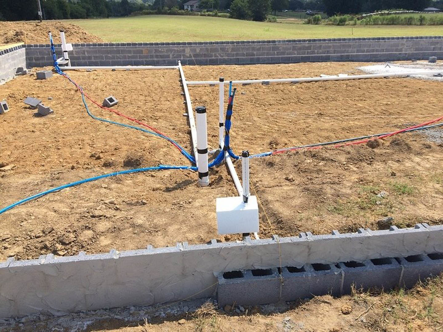 Concrete block wall with holes, white pole featuring blue and red wires, brick wall, and grass visible in the background at a residential construction site.