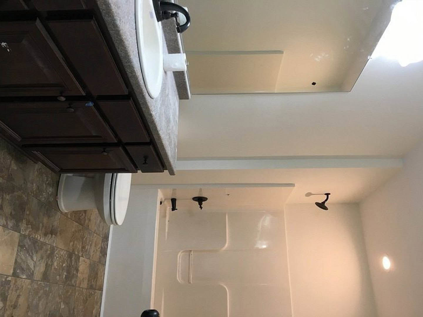 Modern bathroom featuring a white sink with dark wood cabinets, a closed toilet, glass shower enclosure, plaster walls, and a black spiral ceiling light fixture.