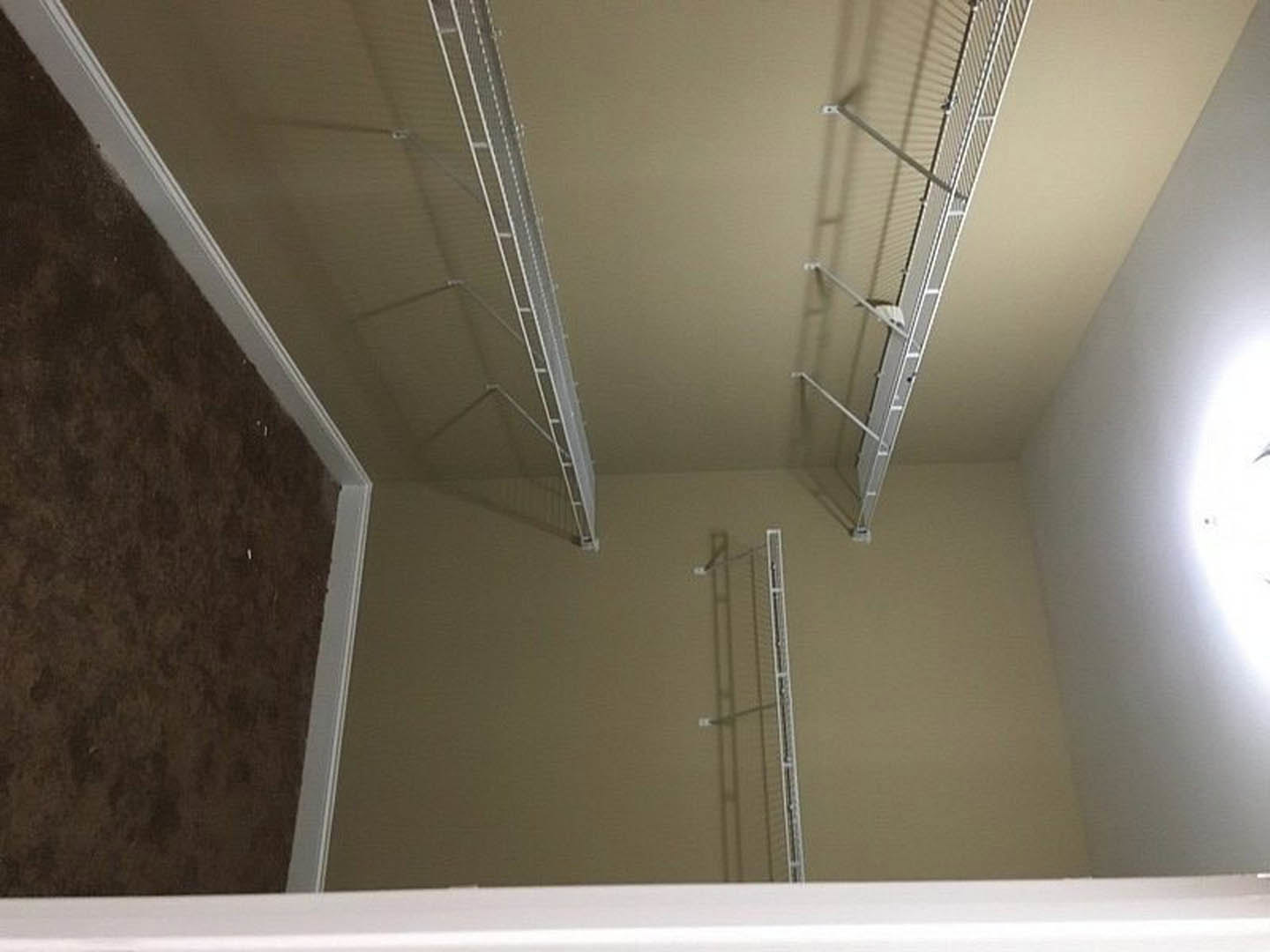 Built-in white shelving along a plaster wall, brown carpet flooring with white baseboard trim, fluorescent ceiling fixture providing overhead lighting