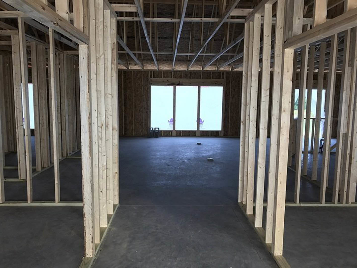Sunlit room featuring a large window, exposed wooden ceiling beams, light-colored walls, and hardwood flooring.