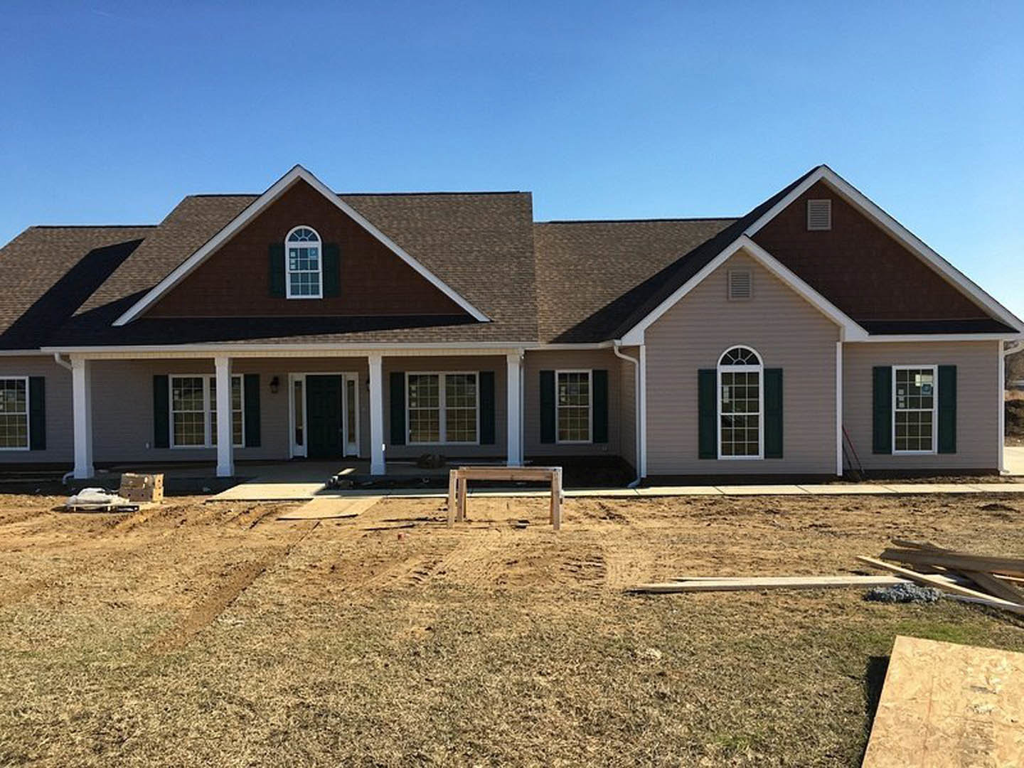 Partially built house with white framed multi-pane windows, large roof, wood siding, and wooden bench in fenced yard