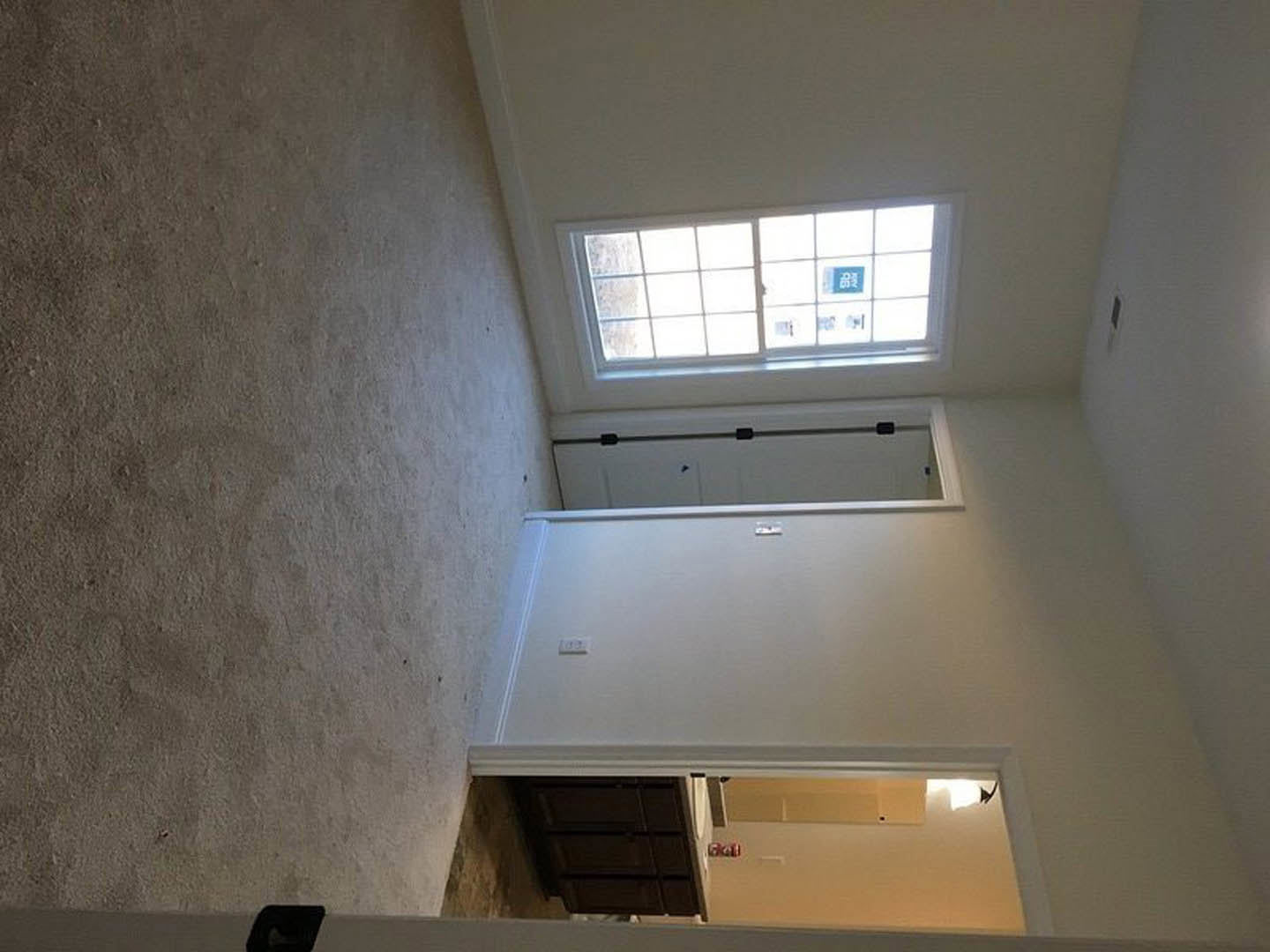 Carpeted room featuring a large window with daylight, white walls, open door, and white cabinetry with drawers