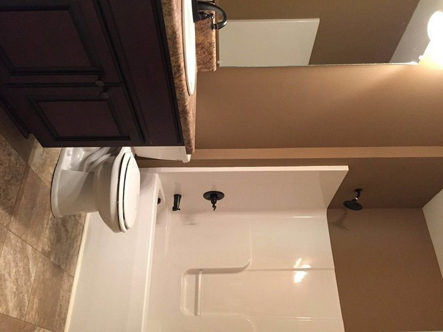 Bathroom with white bathtub and black faucet, black-framed mirror above white sink, black spiral light fixture, close-up of cabinet and exposed pipe, light tile walls and plaster