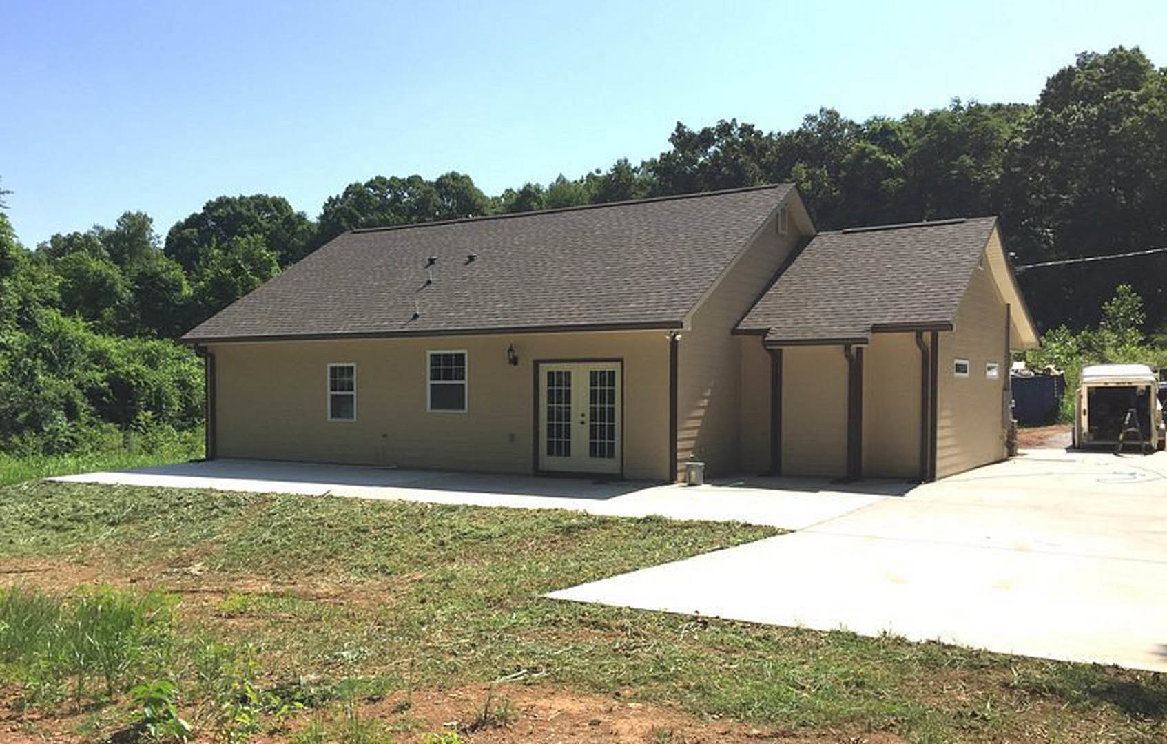 Modern two-story home with gray siding, double front doors, large windows, concrete driveway, green lawn, and a white work truck parked in front