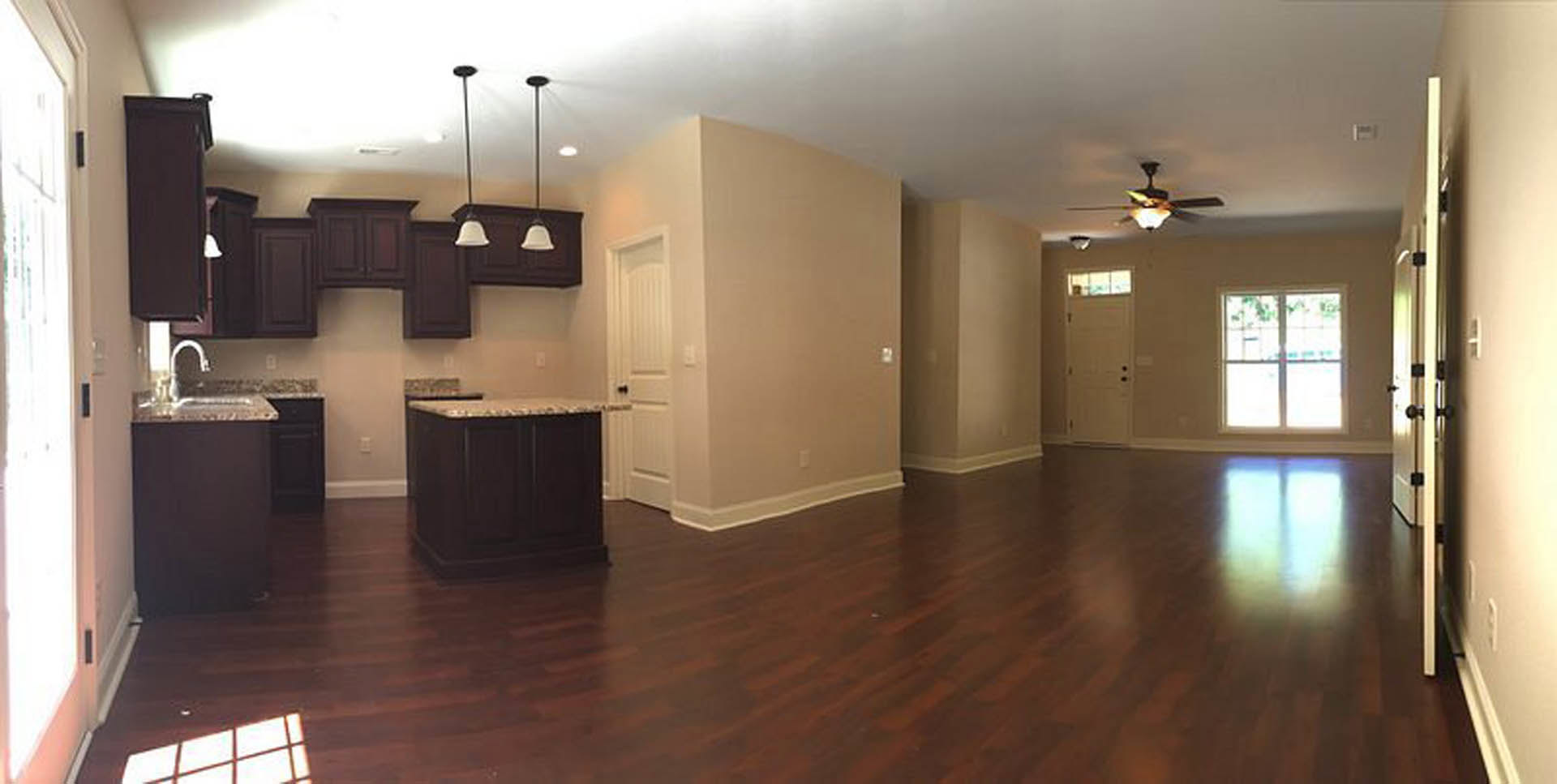 Open living room with hardwood flooring, kitchen island featuring black cabinetry and marble countertop, large window letting in natural light, ceiling fan with light fixture, door