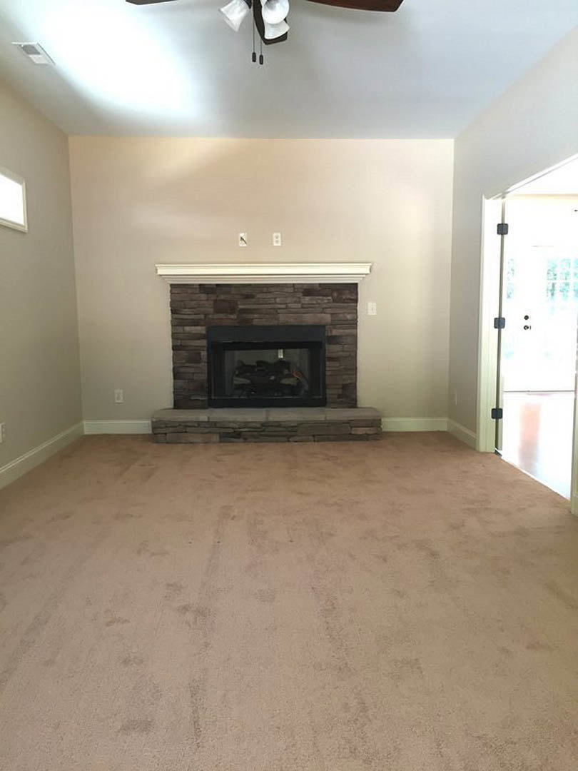 Carpeted living room with plaster walls, glass-front fireplace, ceiling fan, and white door