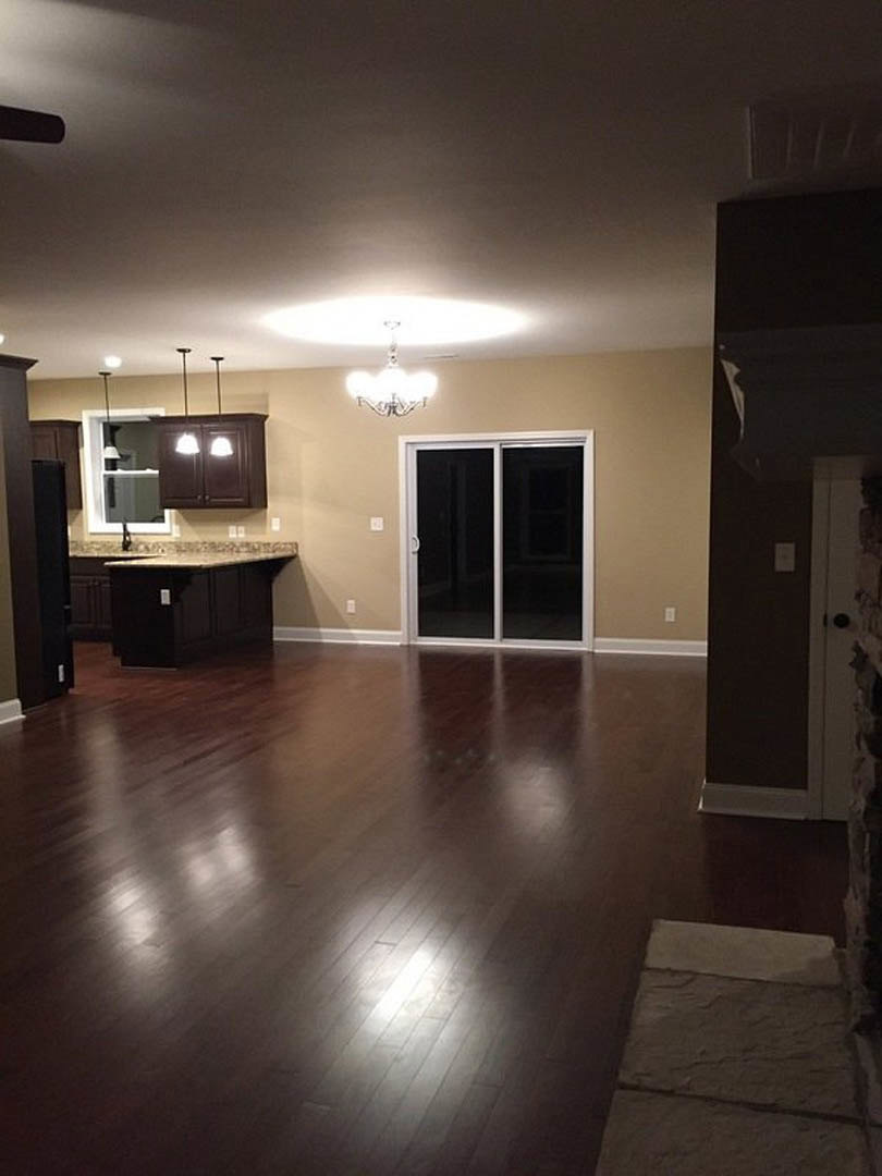 Open living area with hardwood flooring, stone accent wall, modern chandelier, sliding glass door, and large window.