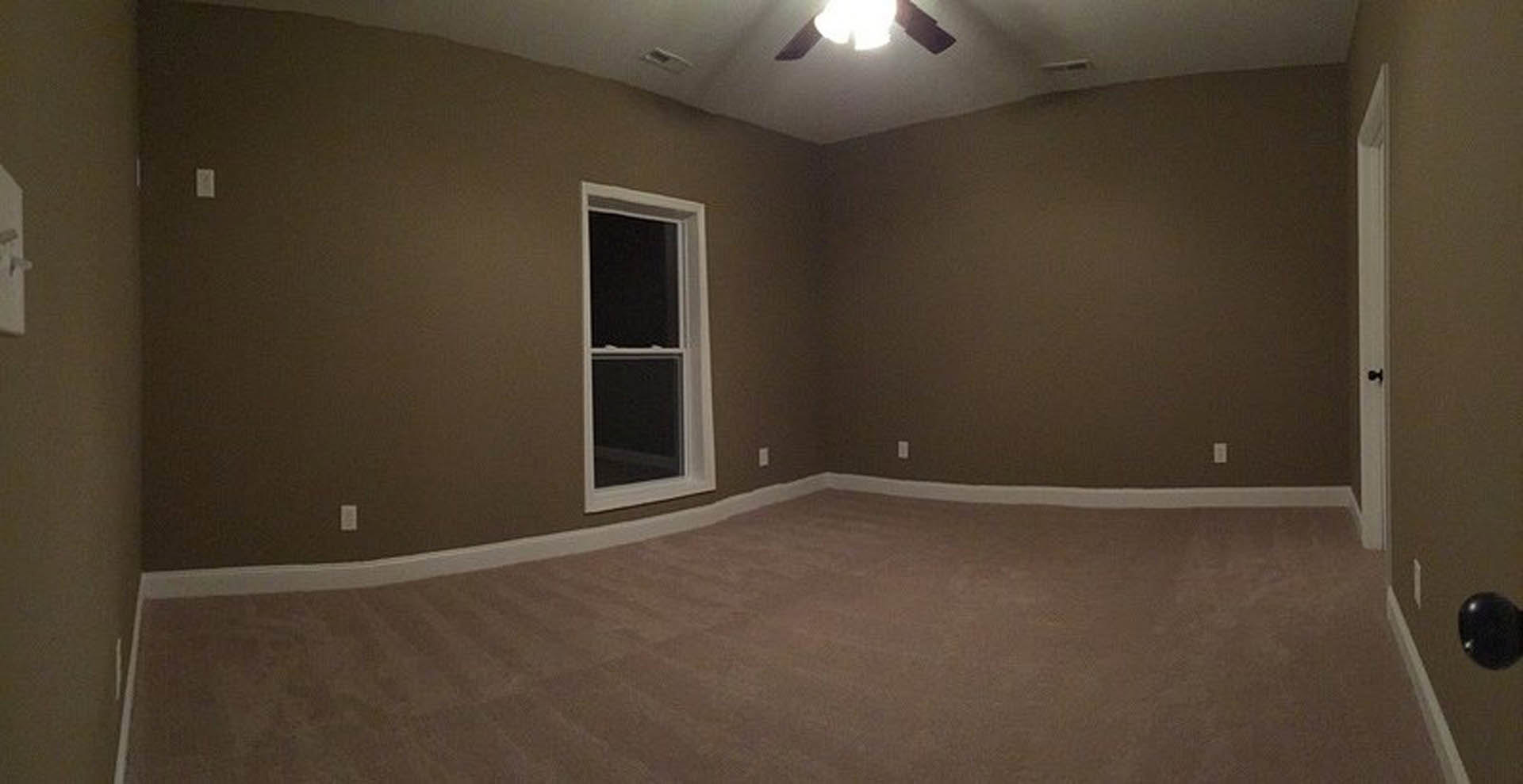 Carpeted room with white-framed window, light fixture in background, blurred person near black reflective object