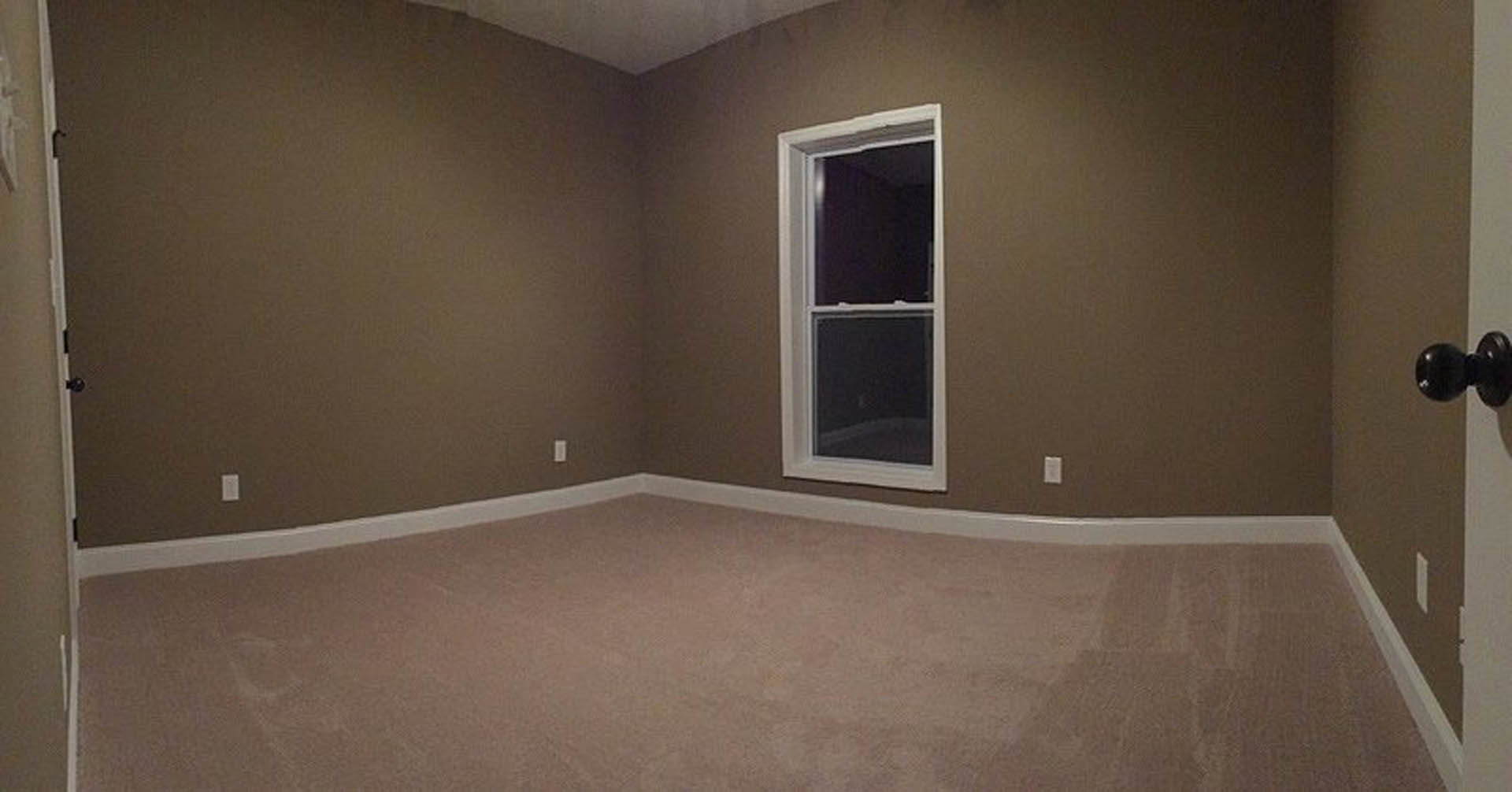 Carpeted room with white walls, large window, and modern door hardware