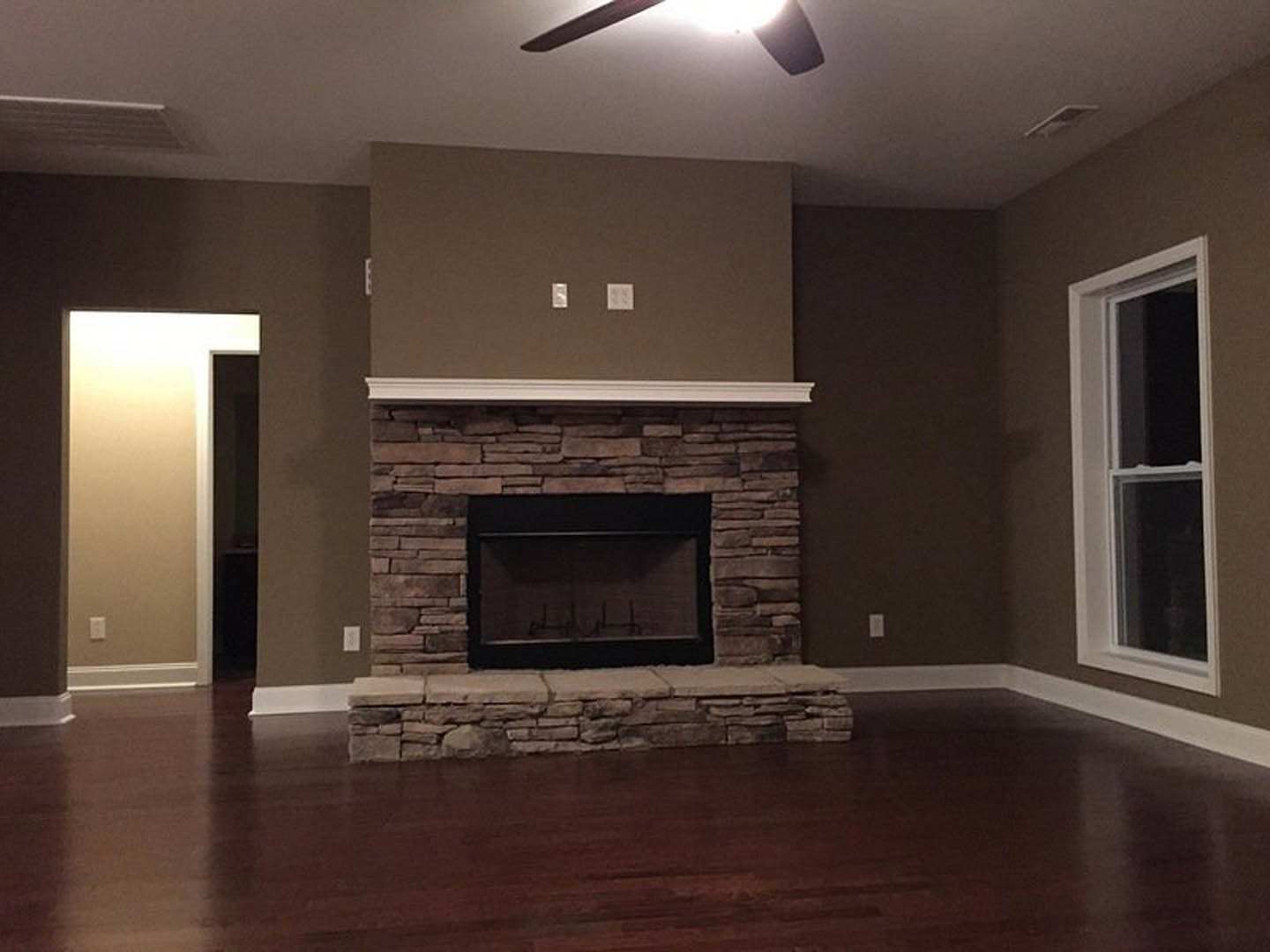 Stone fireplace with black frame, wood flooring, white-framed window, and white ceiling in a modern living room