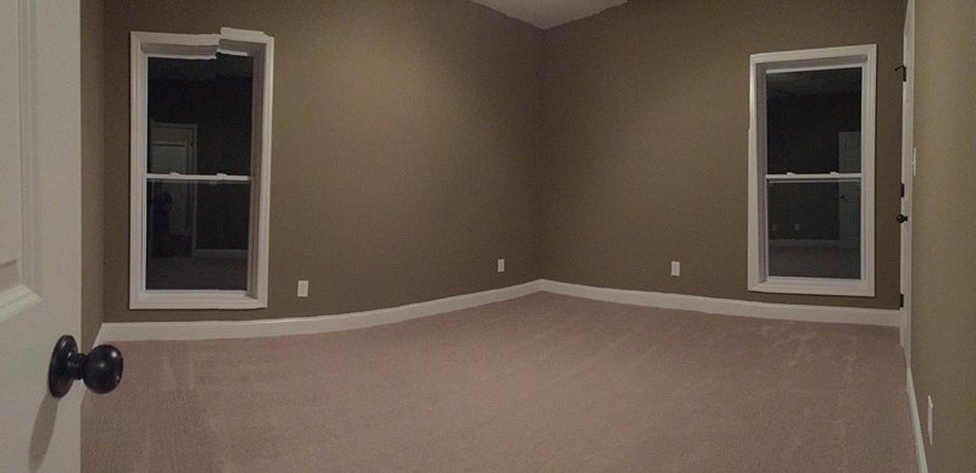 Carpeted room with white walls, large window with white frame, black door knob on white door, natural light illuminating neutral finishes