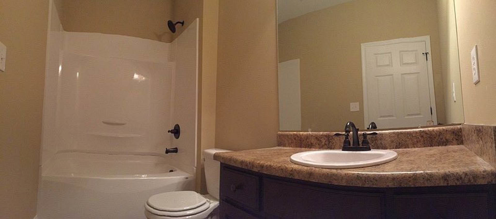 Modern bathroom featuring a white porcelain sink, wall-mounted toilet, glass-enclosed shower, large mirror, and light gray tile walls