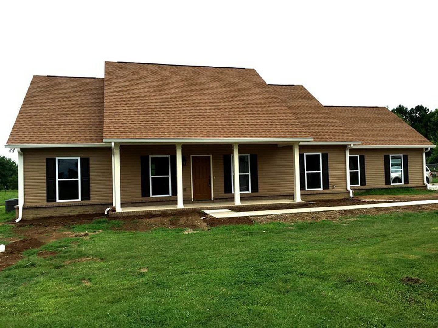 Two-story house with brown roof, white-framed windows, and white porch pillars overlooking a green lawn