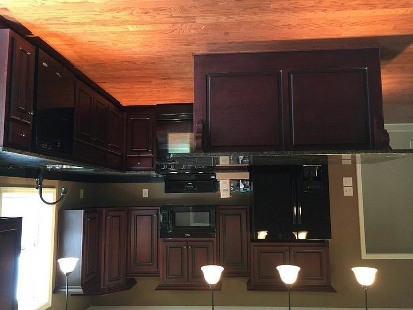 Kitchen featuring dark wood cabinets, wood plank ceiling, black microwave with glass door, round pendant light, and brown cabinetry with black handles