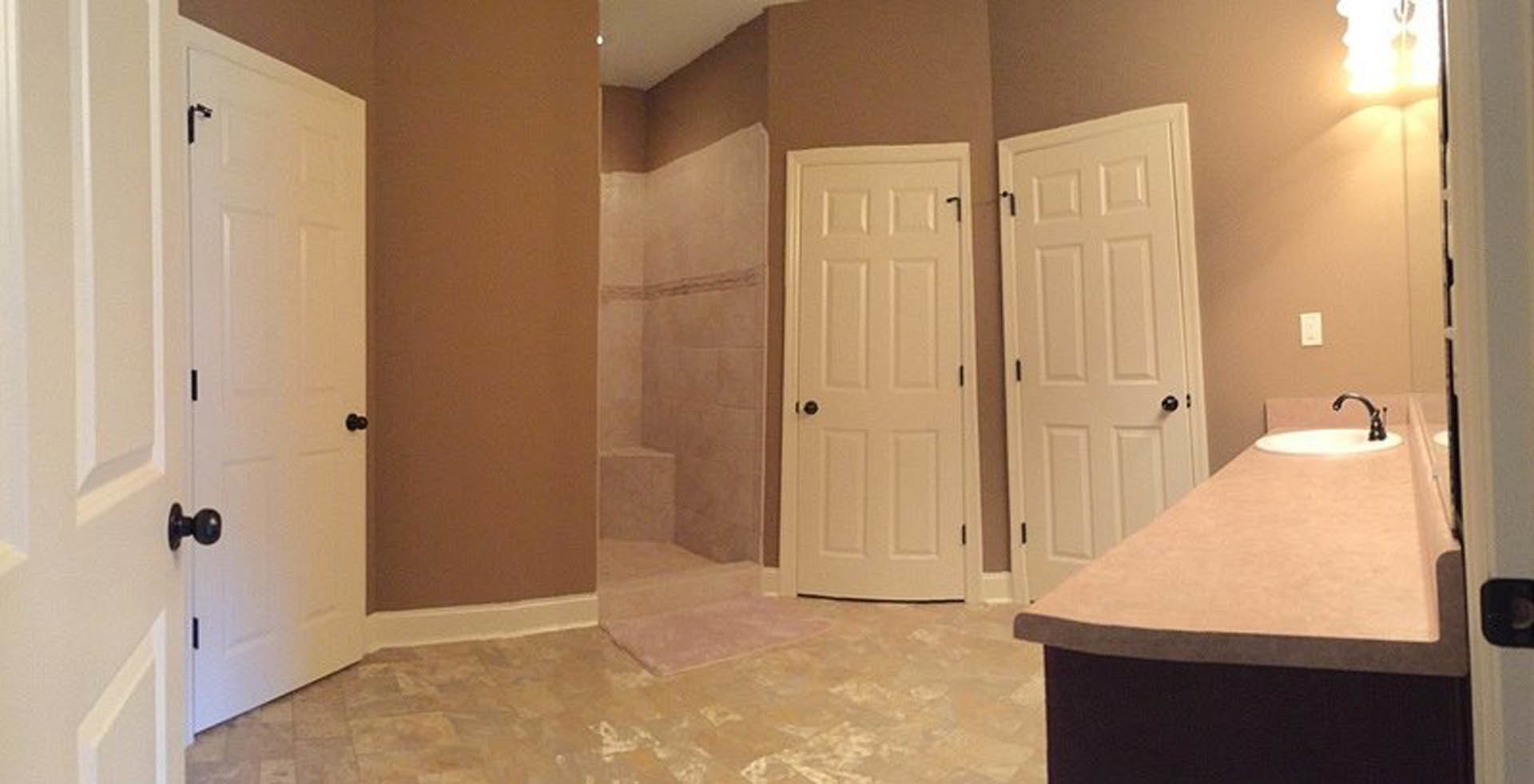 Bathroom with white paneled doors featuring black handles, glass-enclosed shower with tile walls, vanity with sink and mirror, light-colored flooring