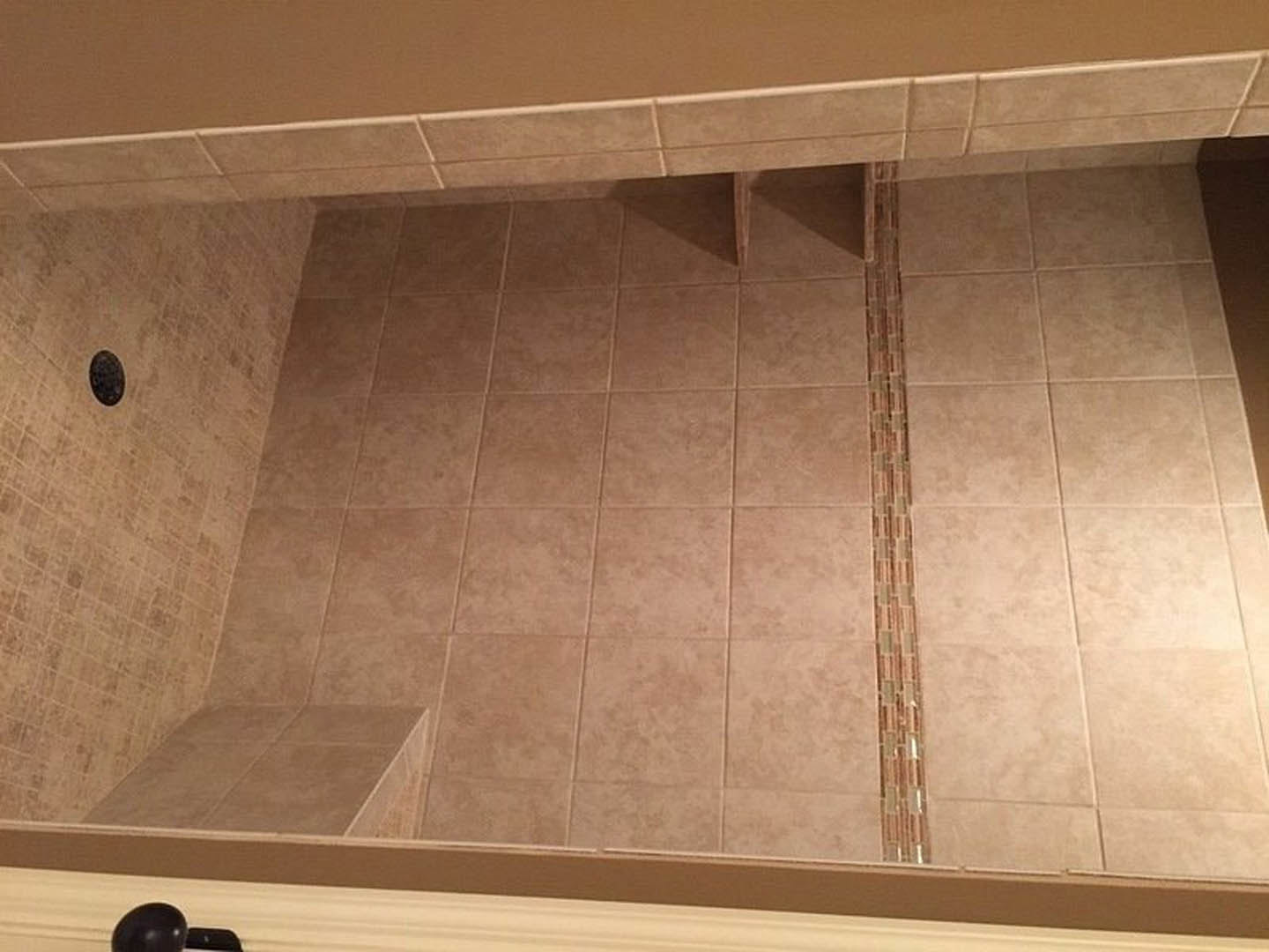 Shower with light-colored tile walls and floor, featuring a close-up of tile edges and a black oval drain on a white surface.