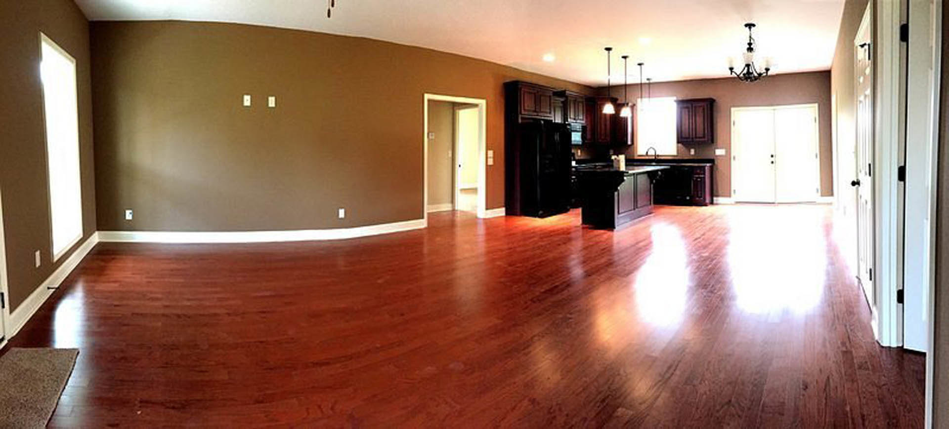 Open-concept kitchen and living room featuring hardwood floors, white walls, recessed lighting, and large windows with red curtains