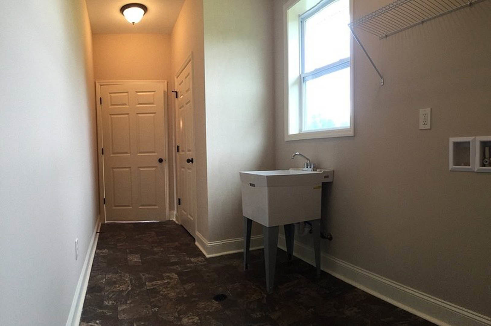 Bathroom with white sink and chrome faucet, rectangular window above, white tile walls, black hardware on white door, square shelf with glass inset, visible electrical outlet.