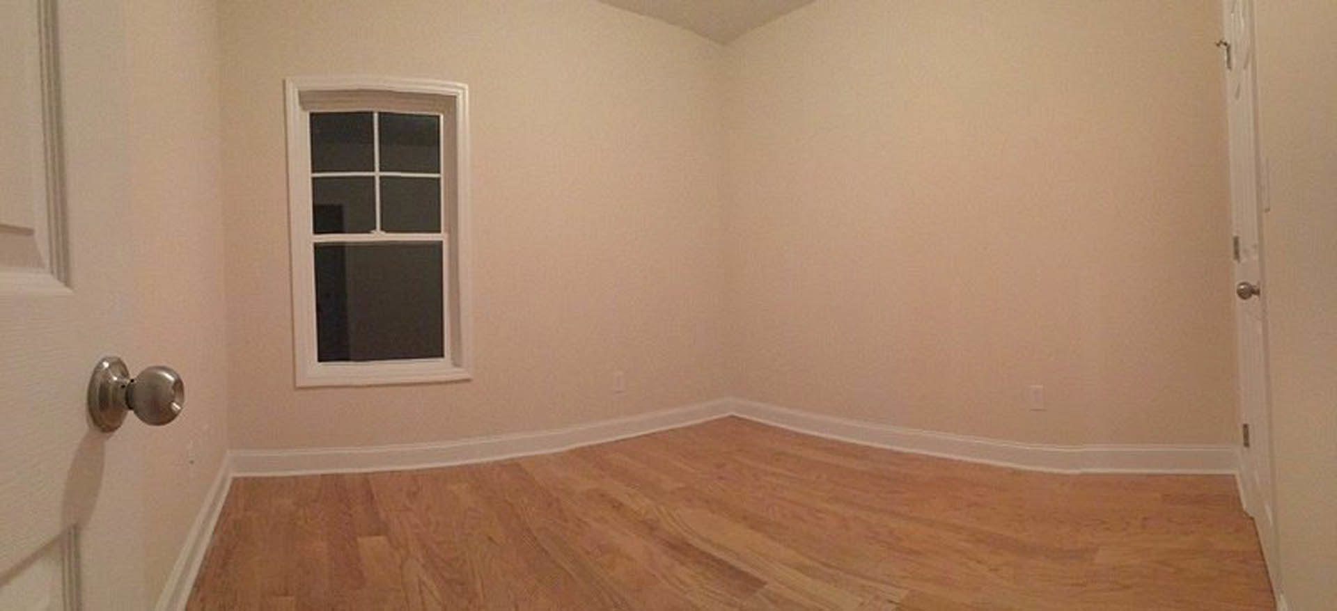 Hardwood floor with white baseboard trim, white-framed window, plaster walls, and close-up of brushed metal door knob