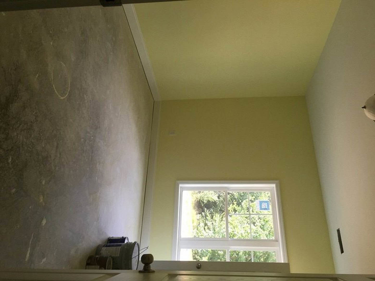 Yellow plaster wall with a window featuring a blue sign, white ceiling, and indoor lighting fixture in a residential interior.