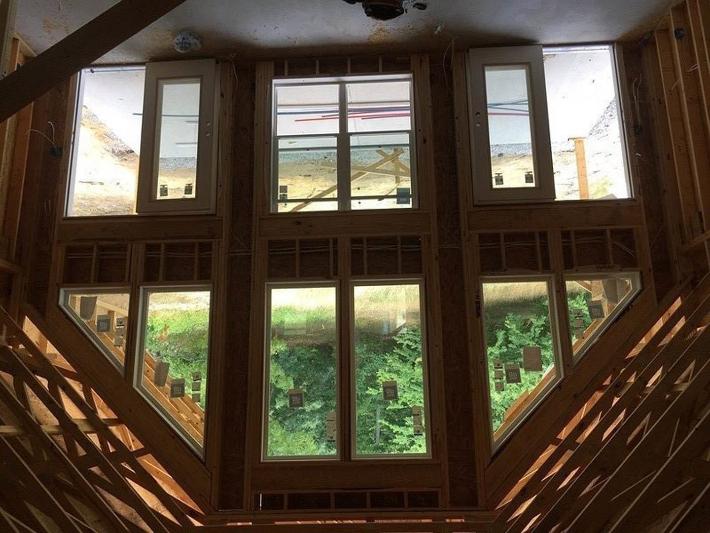 Wood staircase with large windows, broken glass pane, white door, and ceiling view; trees visible outside through windows