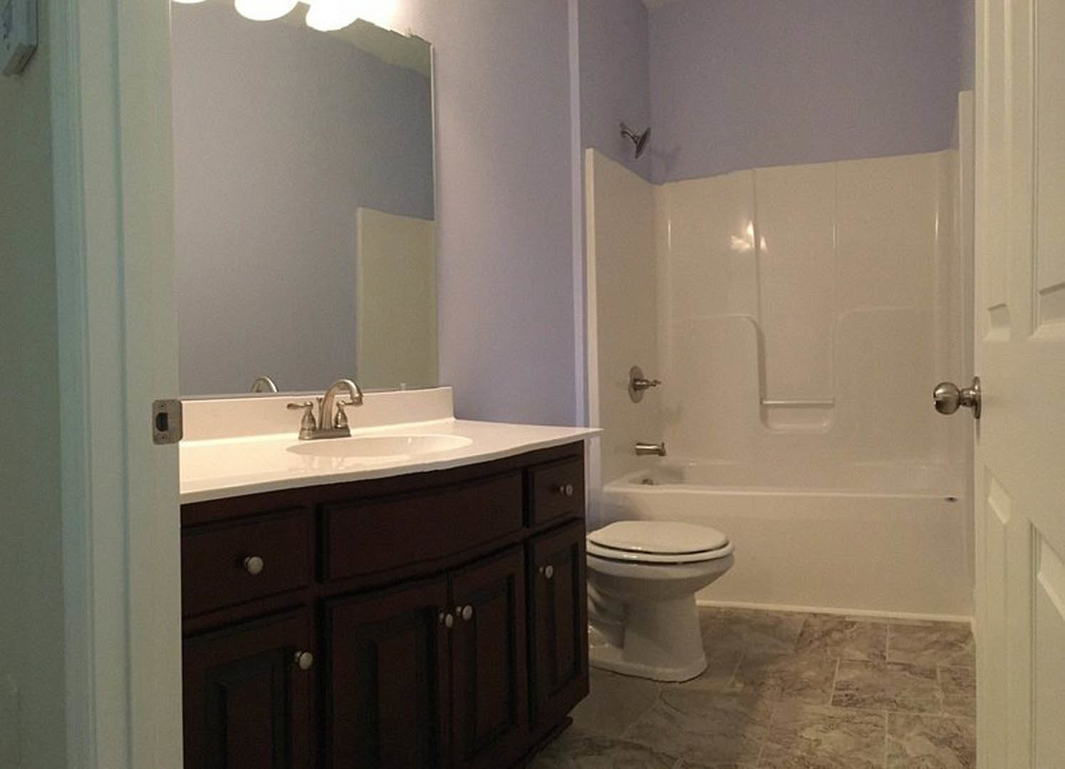 Modern bathroom with white porcelain sink, closed toilet, glass shower enclosure, chrome fixtures, white trash can, and light tile flooring