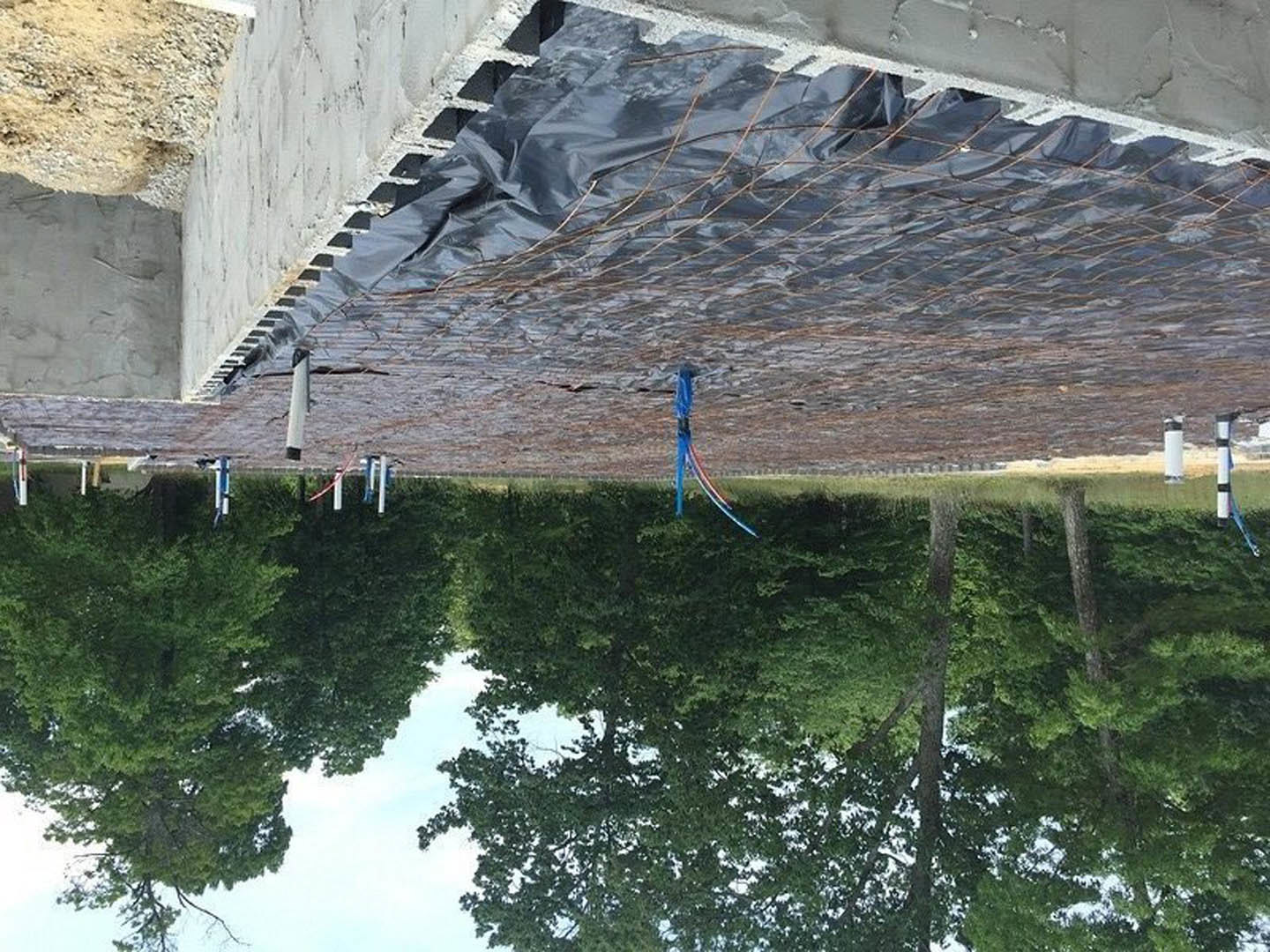 Black tarp draped over partially constructed building in tree-lined yard with playground equipment and blue pole nearby