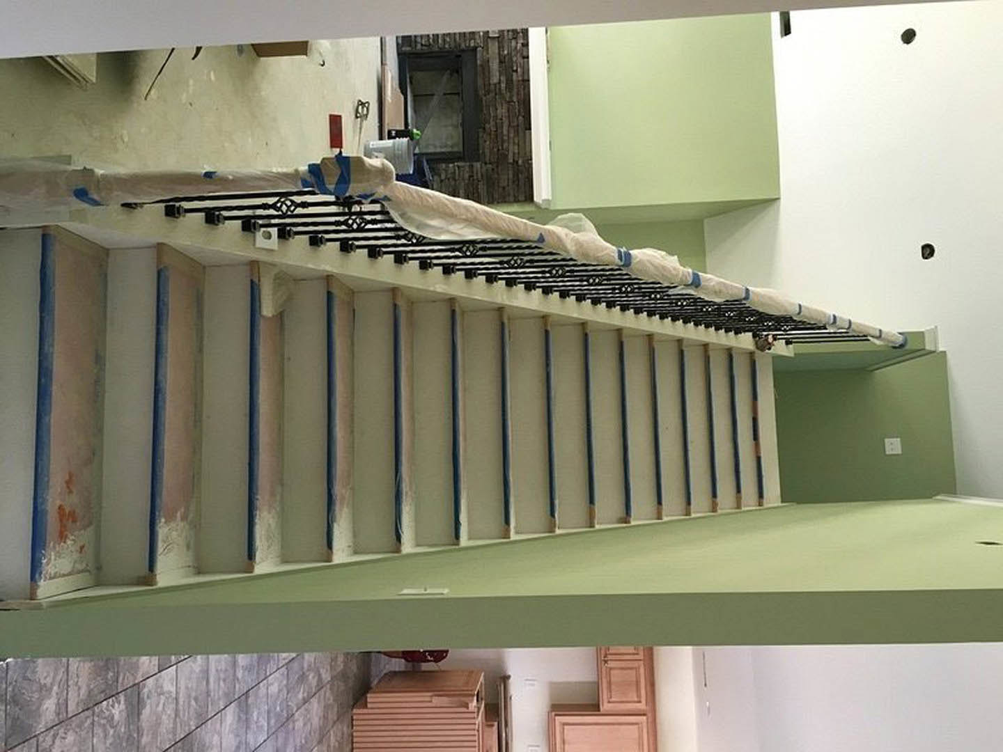 Blue-painted iron staircase with white protective covering, adjacent to a green wall and window.