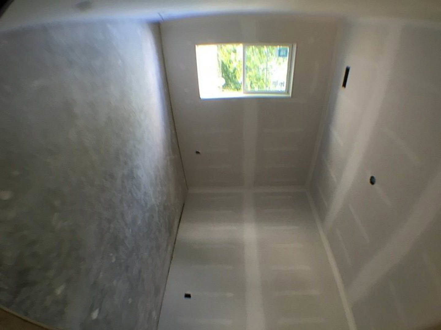 White bathroom with plaster walls, large window, and smooth grey concrete accent wall under natural daylight