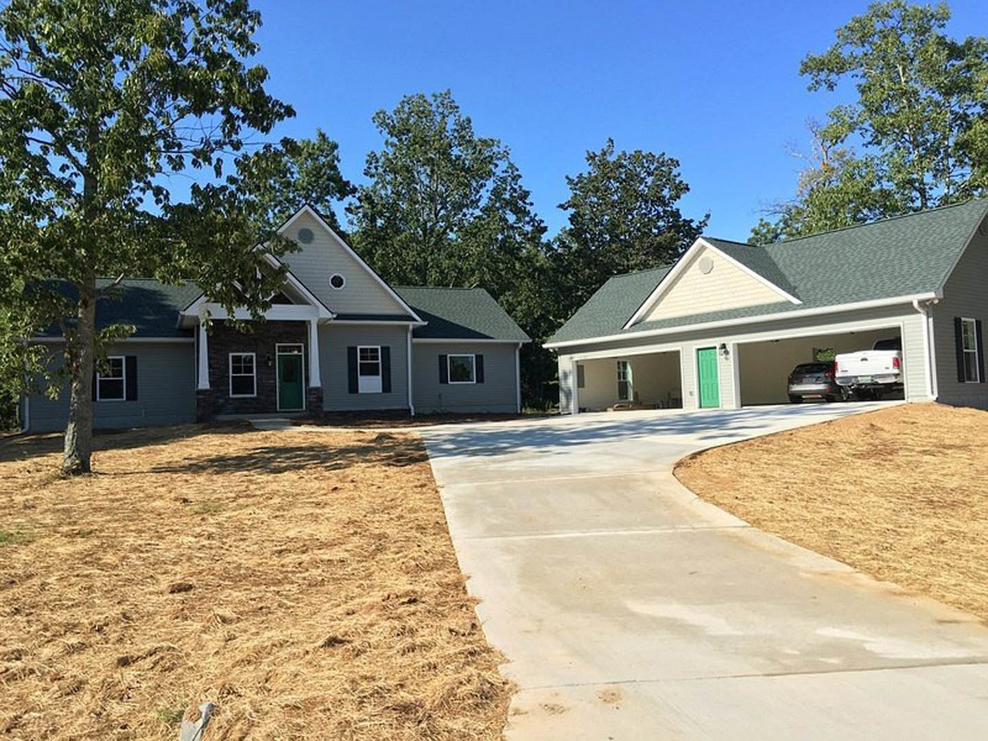 Two-story house with white siding, green front door with window, attached garage, concrete driveway bordered by grass, parked car, large front window with white frame, mature tree