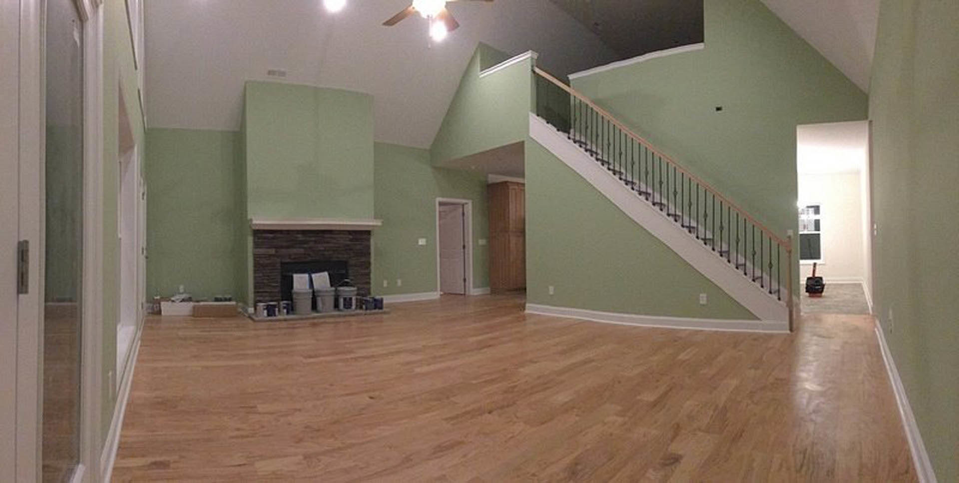 Open living area with wooden floors, metal-railed staircase, white plaster walls, and modern fireplace