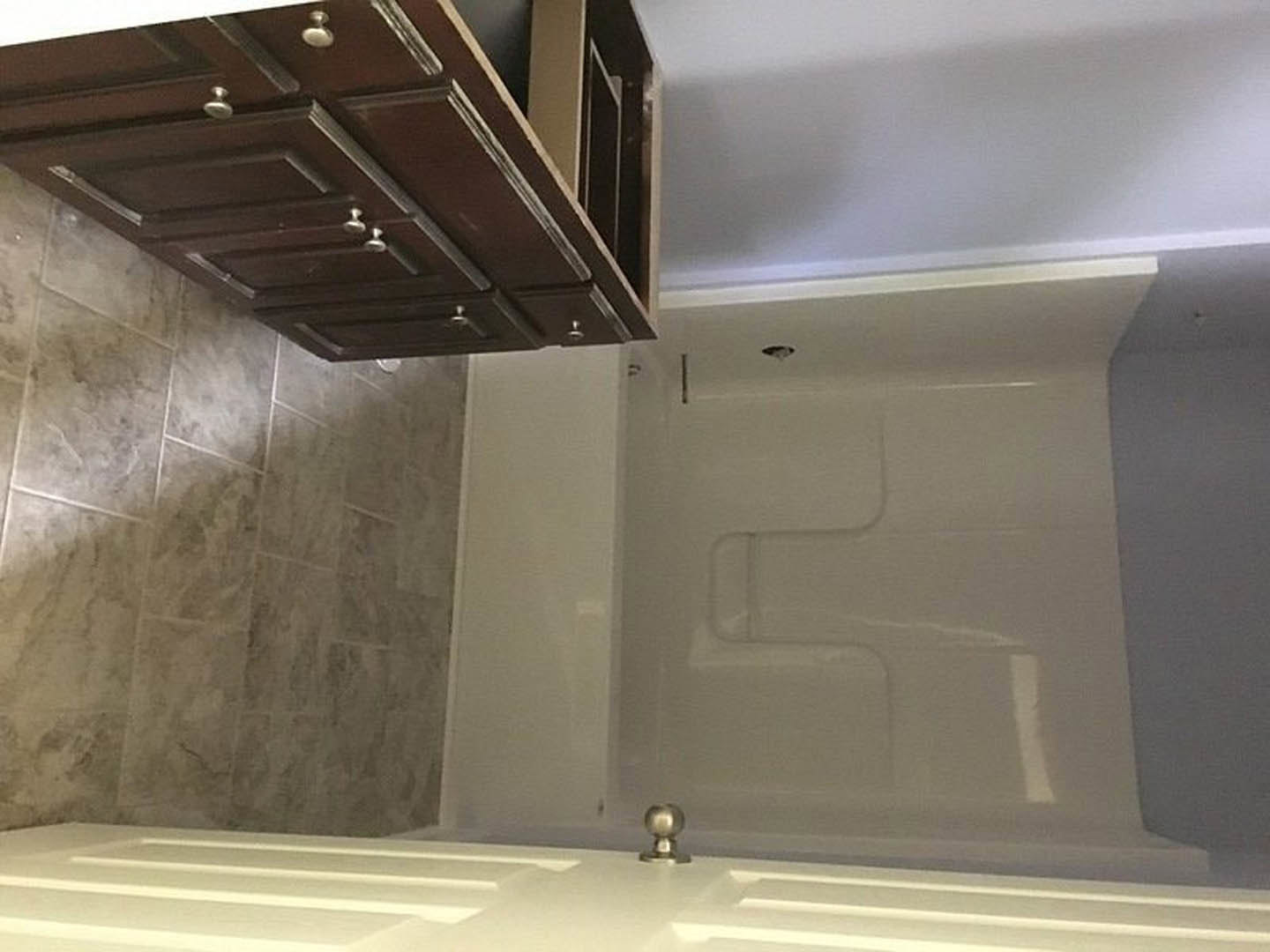 Bathroom with white tile floor, dark wood vanity cabinet with silver knobs, white sink, freestanding bathtub, white walls, chrome faucet fixtures.