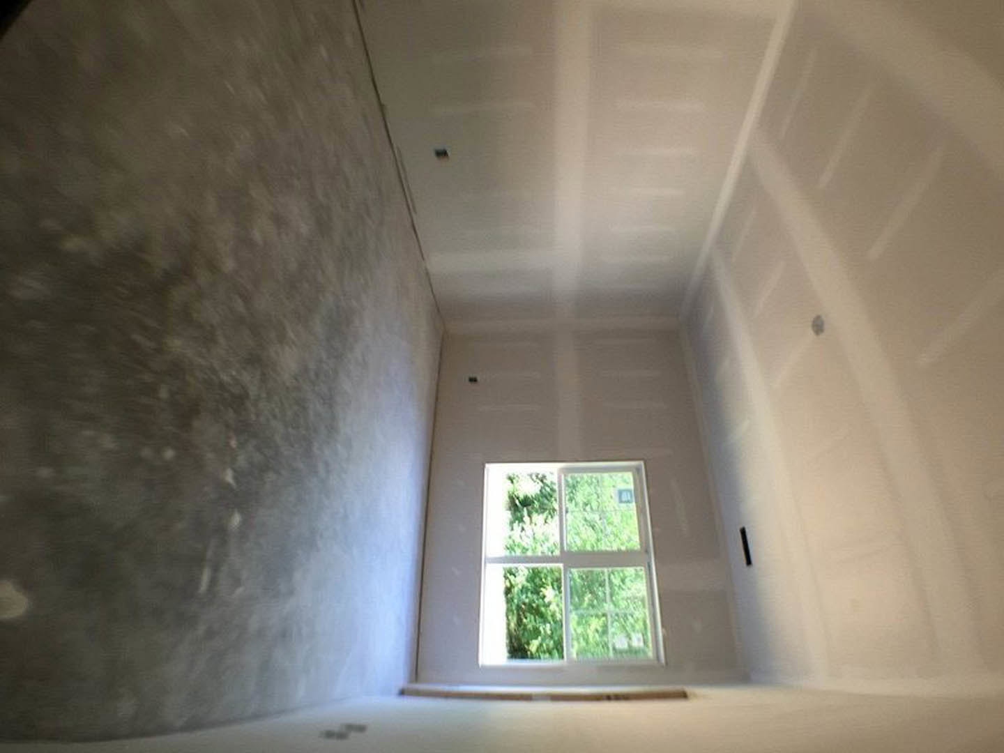 Sunlit room with plaster walls, large window overlooking trees, concrete floor, and ceiling fixture