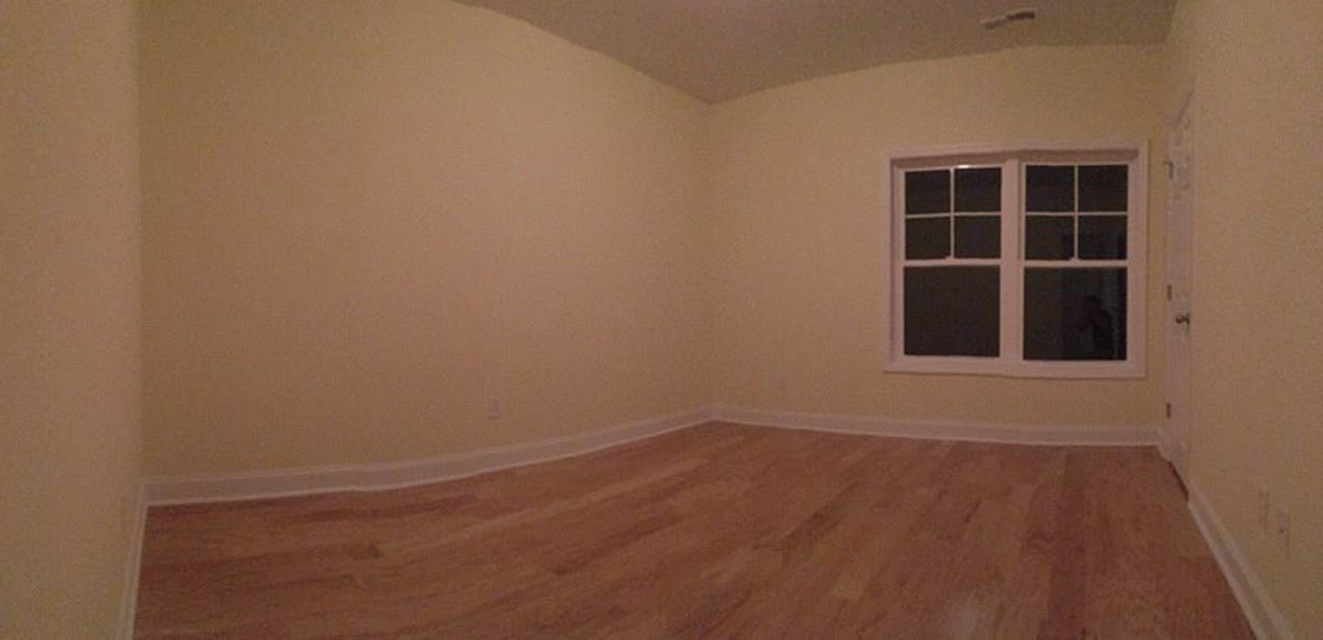 Sunlit room featuring multi-pane window, smooth hardwood flooring, white plaster walls, and ceiling with partial view of doorway.