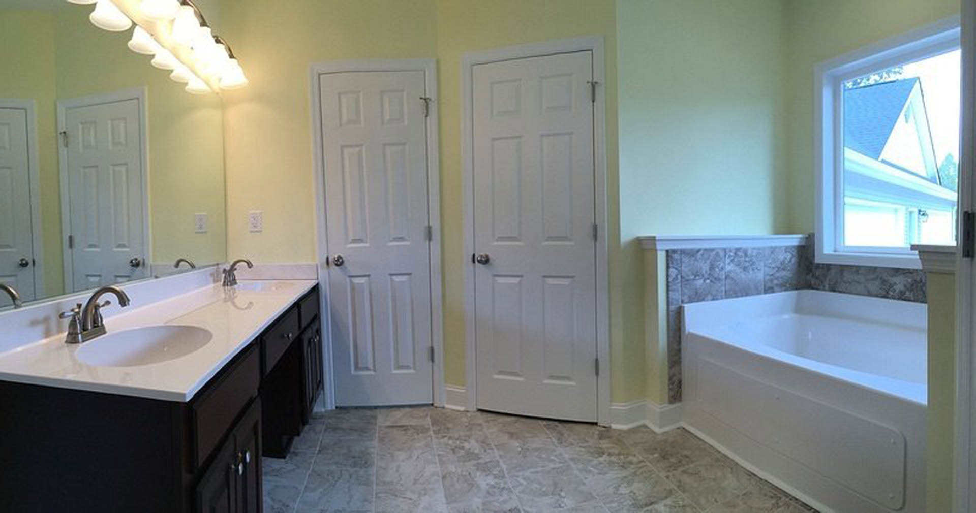 Bathroom featuring white paneled doors, freestanding bathtub, tiled walls, modern sink with chrome faucet, and contemporary light fixture