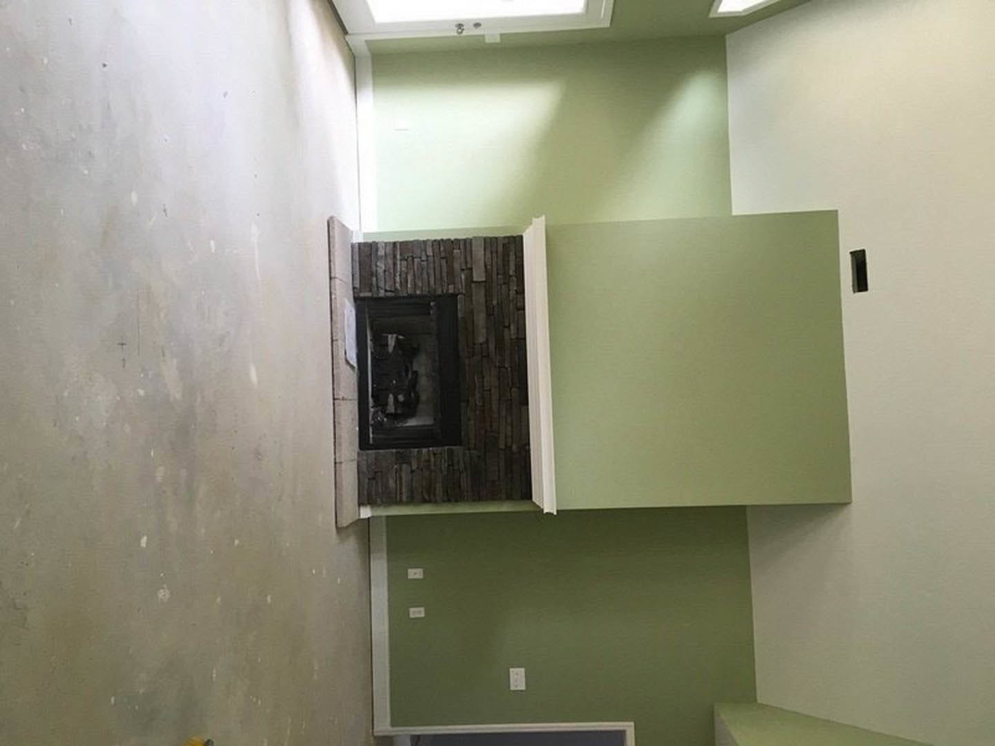 Brick fireplace set into a green wall with white trim, white ceiling, and visible electrical outlet in a residential living room
