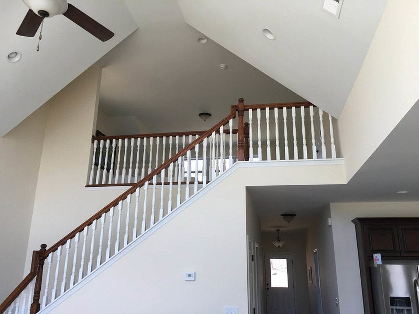 Wood staircase with white railings and balusters, adjacent to a white door with glass window, light fixture hanging from ceiling, refrigerator partially visible, walls finished in