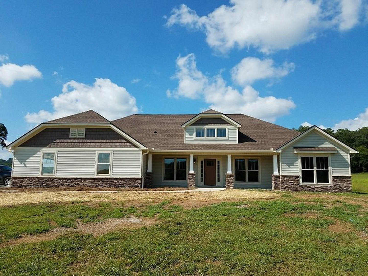 Two-story house with brown roof, white-trimmed windows, brick walls, brown front door, and manicured green lawn under clear blue sky