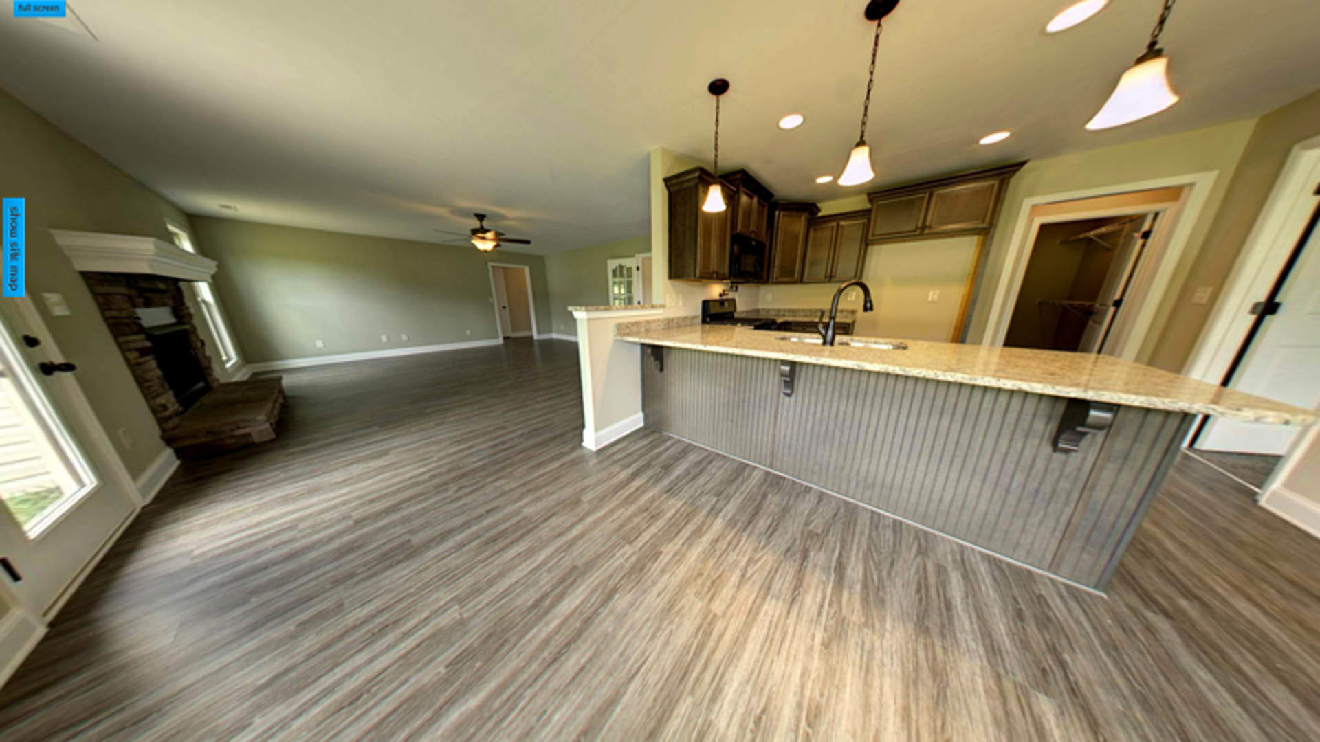 Open-concept kitchen and living room with hardwood floors, white cabinetry, stone countertop with built-in sink, modern pendant lighting, and a fireplace with tile surround.
