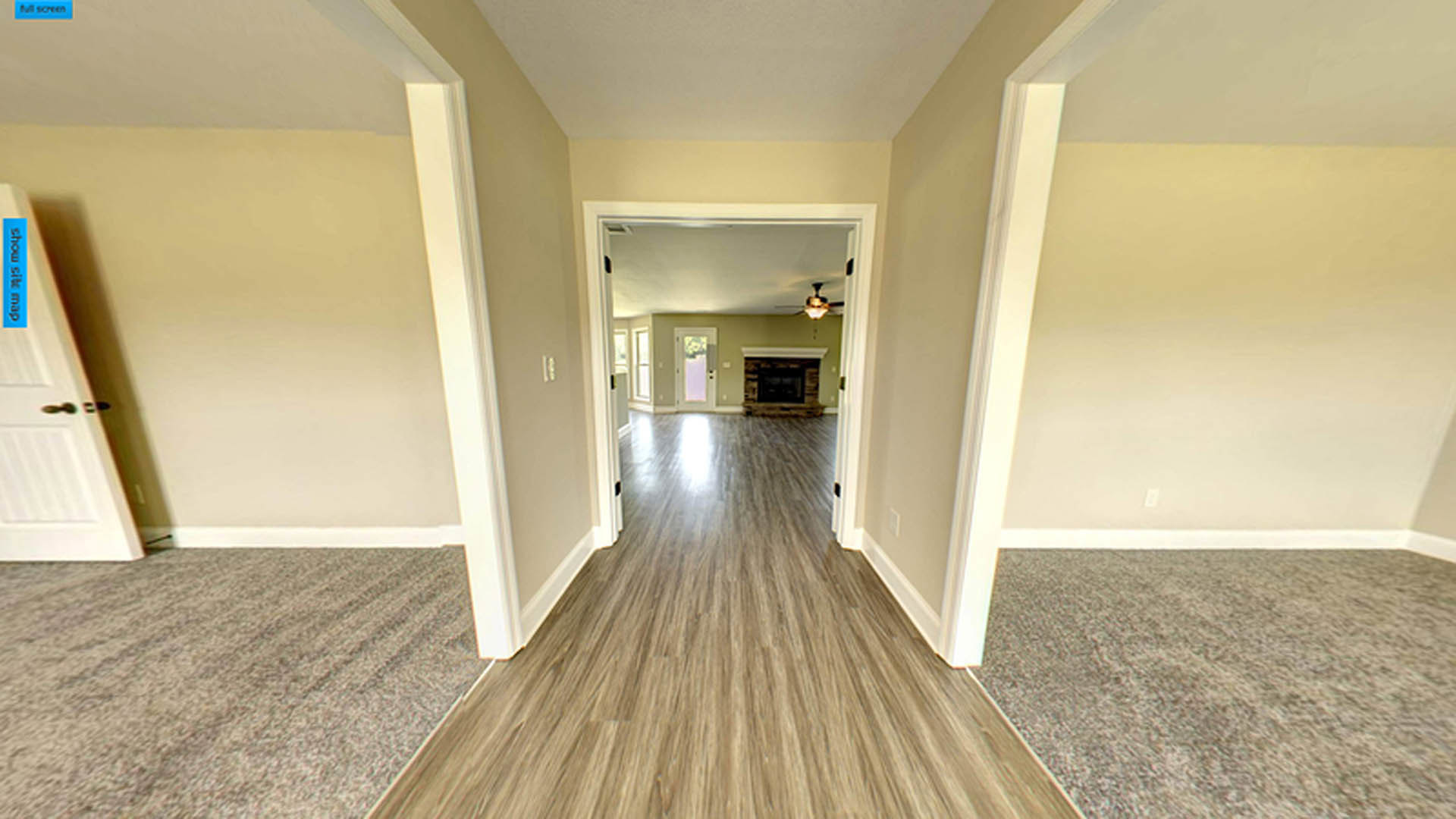 Hallway with medium-toned wood flooring, white plaster walls, built-in fireplace, and a door at the end