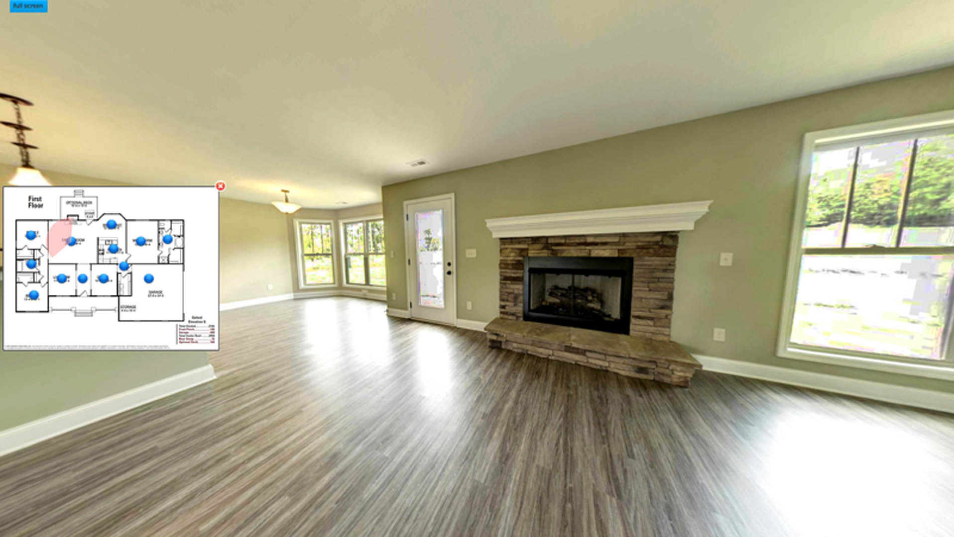 Living room with black glass-door fireplace, wide window overlooking trees, hardwood flooring, white walls, and wood trim.