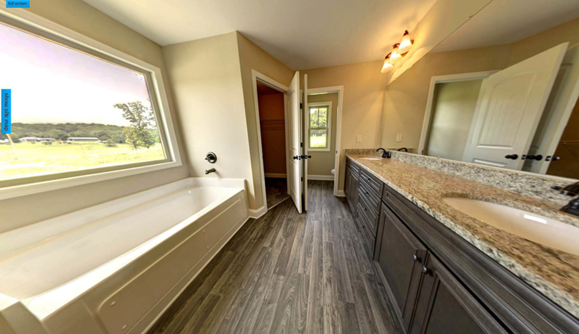 Bathroom with freestanding bathtub, granite countertop sink, wood flooring, white shelving, large window overlooking field, and open white door with glass panel