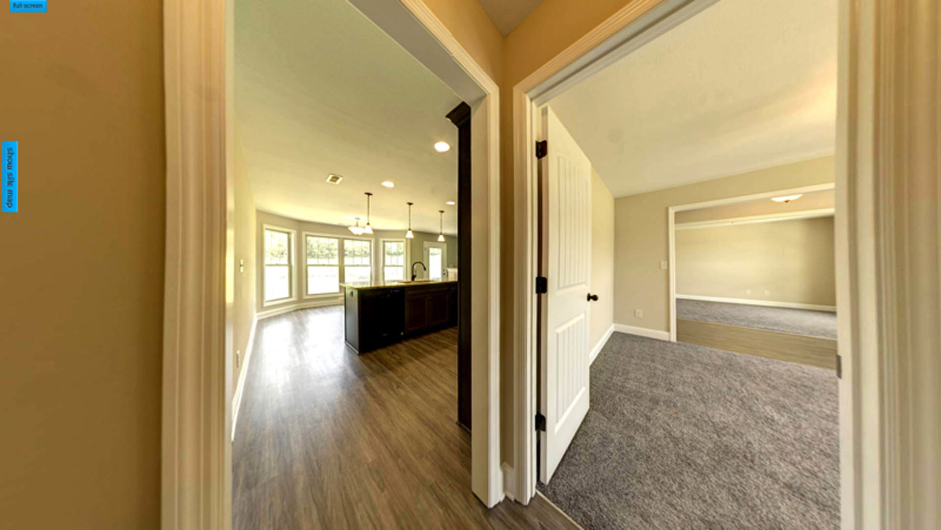 Hallway with carpeted floor leading to open door, kitchen counter with sink beneath window, plaster walls, ceiling molding, and blurred kitchen area in background