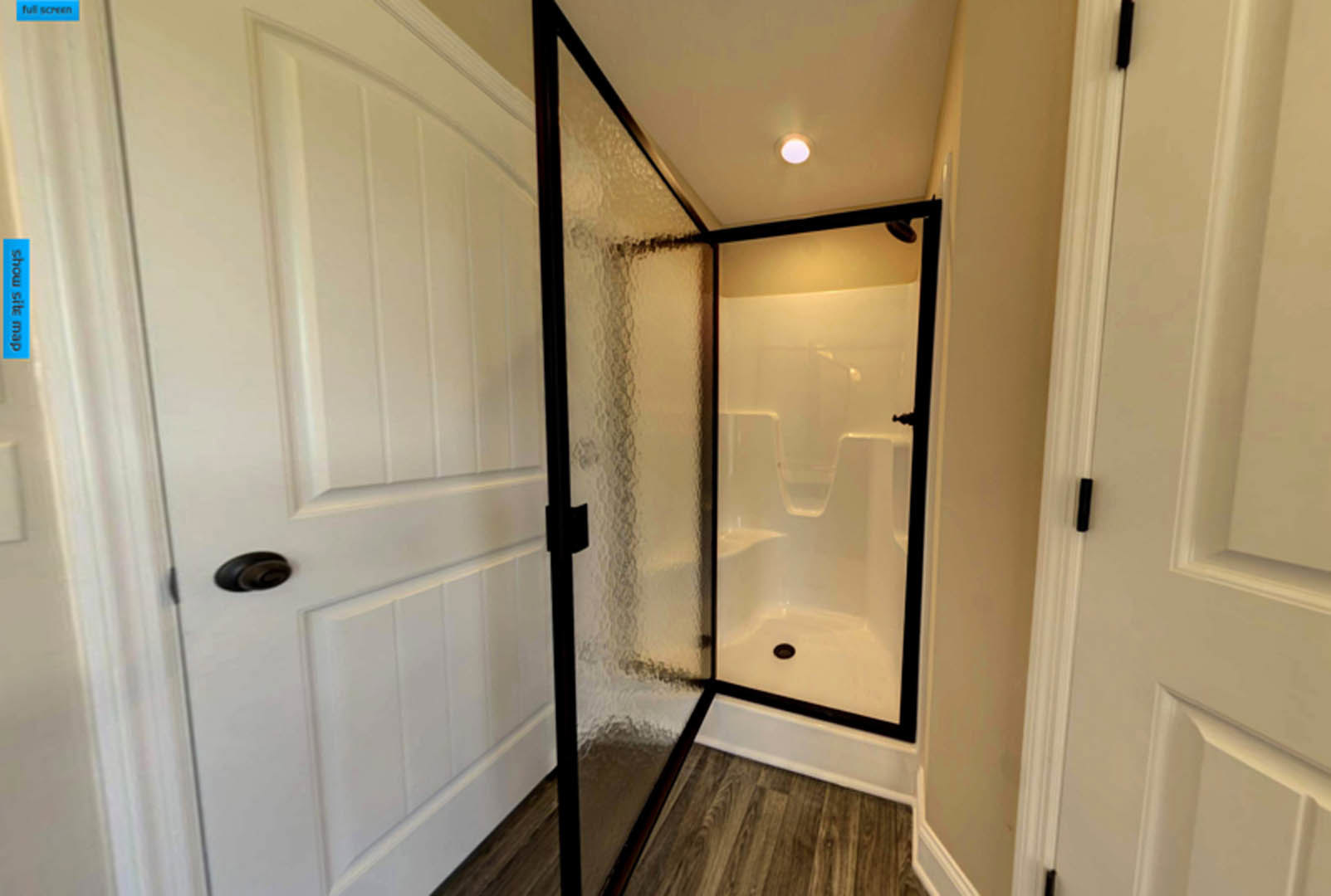 Walk-in shower with clear glass doors, white tile walls, black hardware, recessed ceiling light, and adjacent white door with black handle