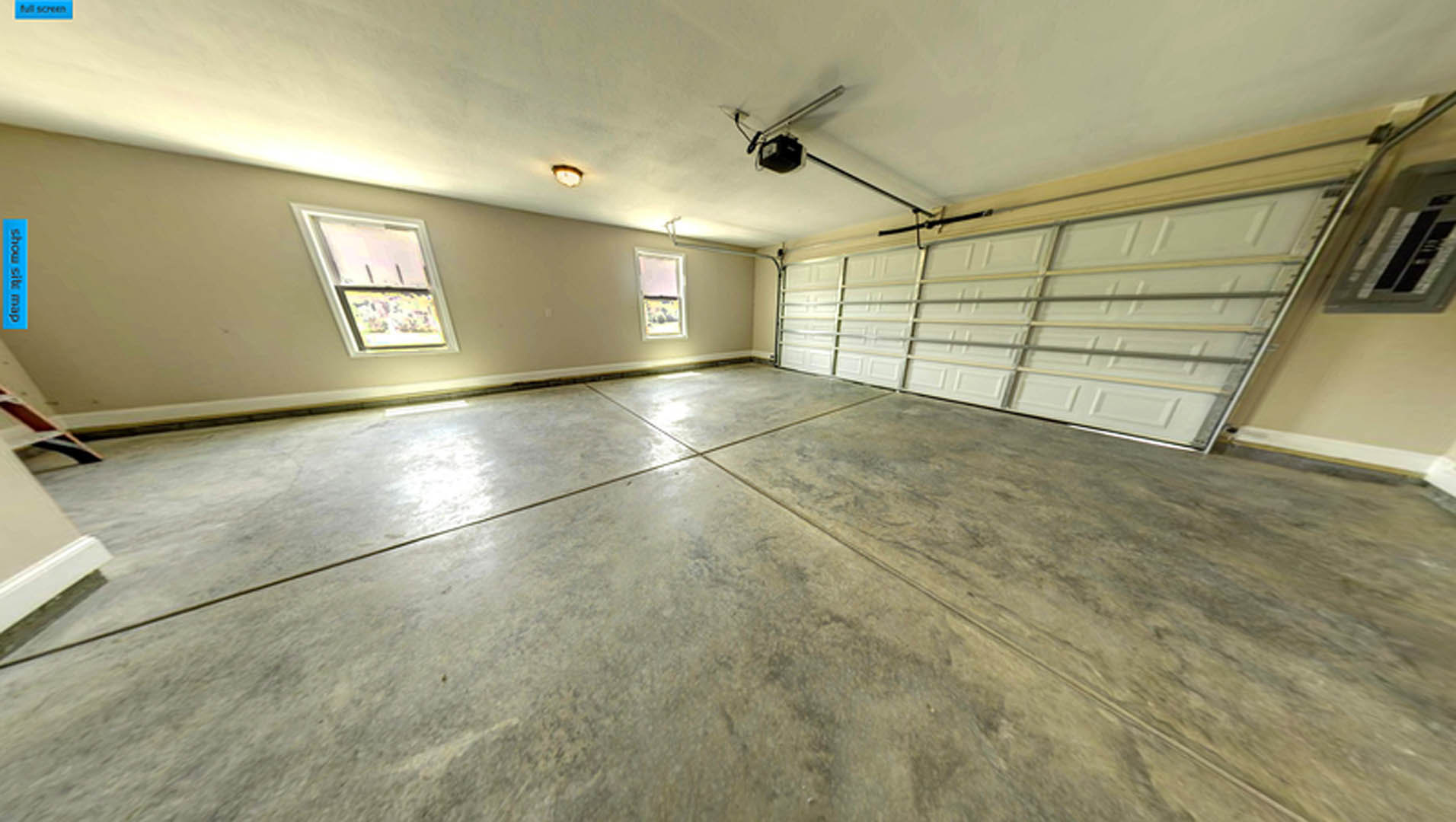 Spacious empty garage with smooth concrete floor, white plaster walls, several windows with white frames, and exposed metal bars on the garage door