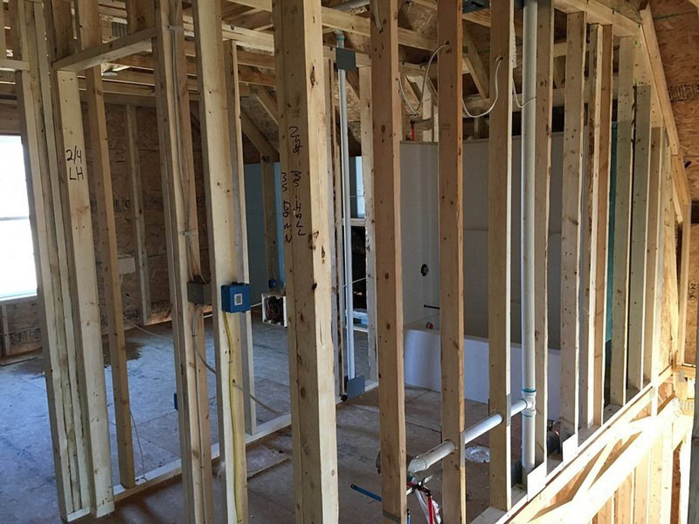 Exposed wooden framing and beams inside a house under construction, with insulation visible between studs and a temporary sign attached to the structure