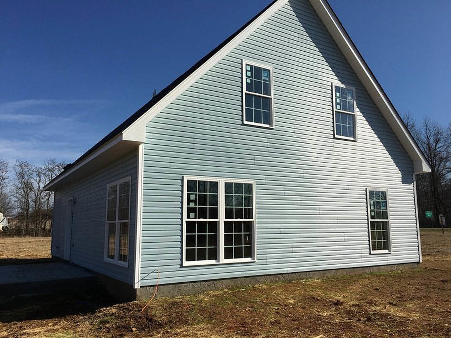 Two-story home with blue metal roof, white-framed windows, light gray siding, and mature tree in front yard