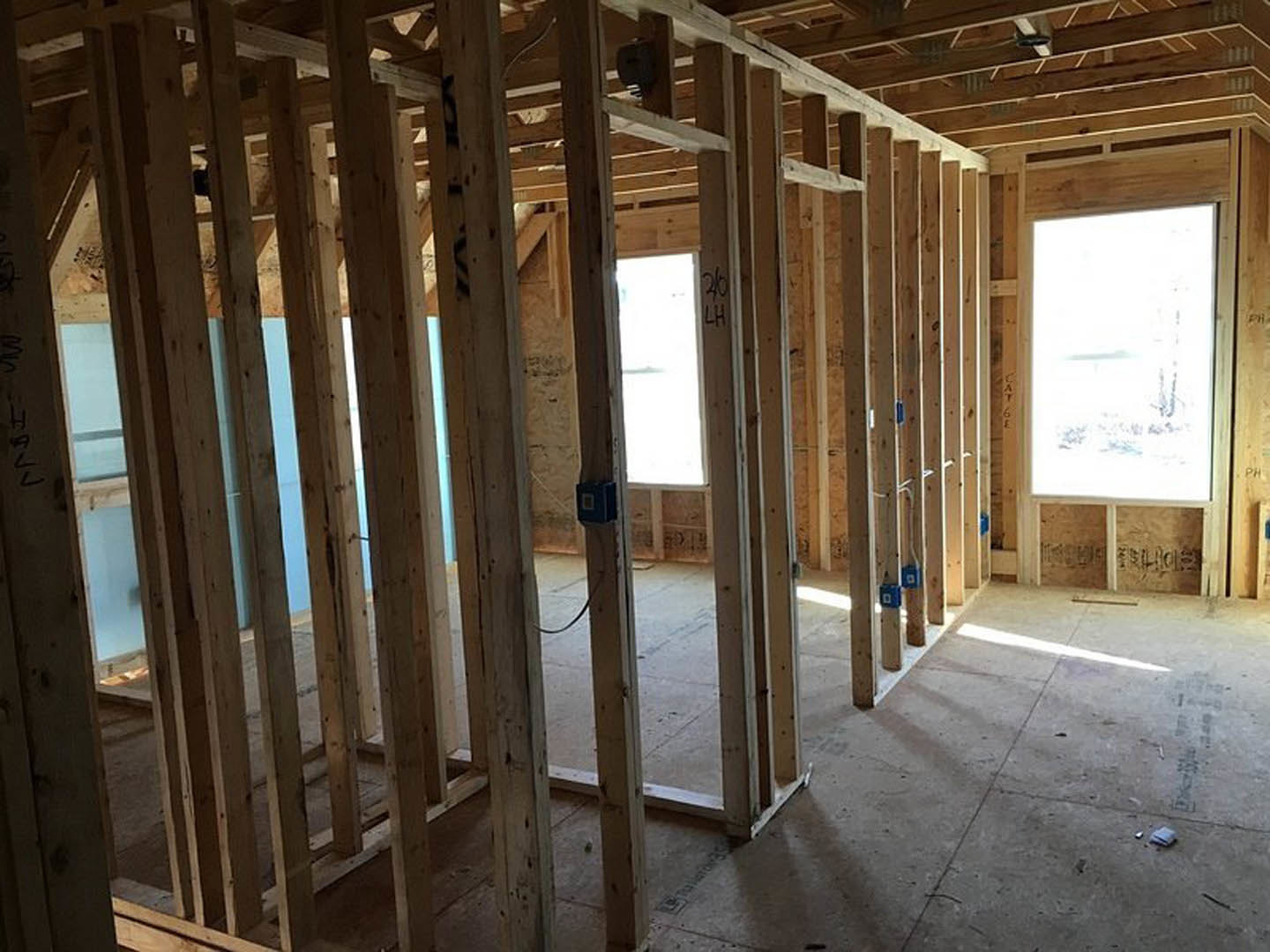 Wood-framed room under construction with exposed beams, concrete floor, black box structure featuring a square window, blue sign on floor, window overlooking snowy landscape and